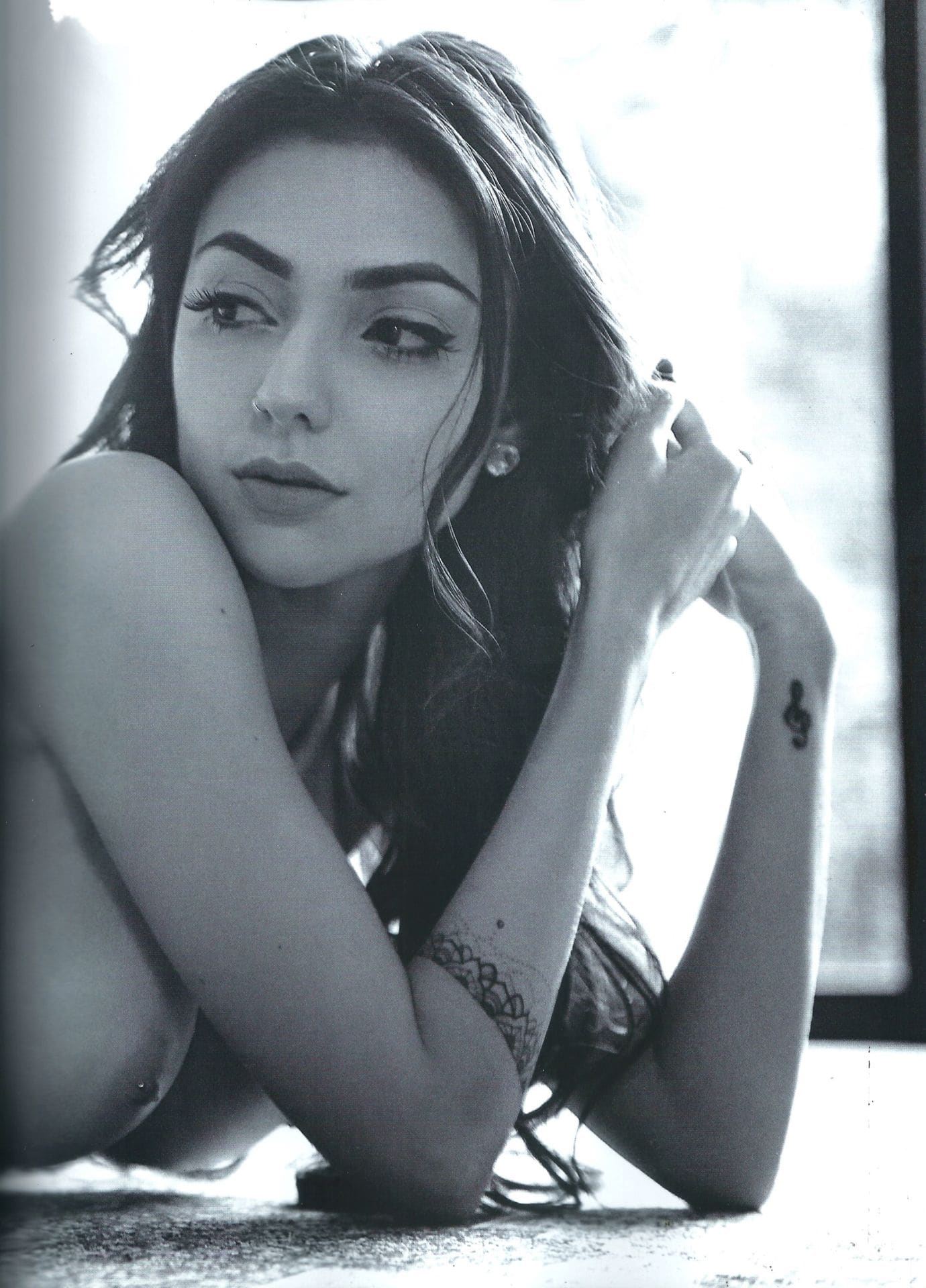 A black-and-white portrait shows her sitting on the floor in a lace top, arms around her knees, near a bright window.