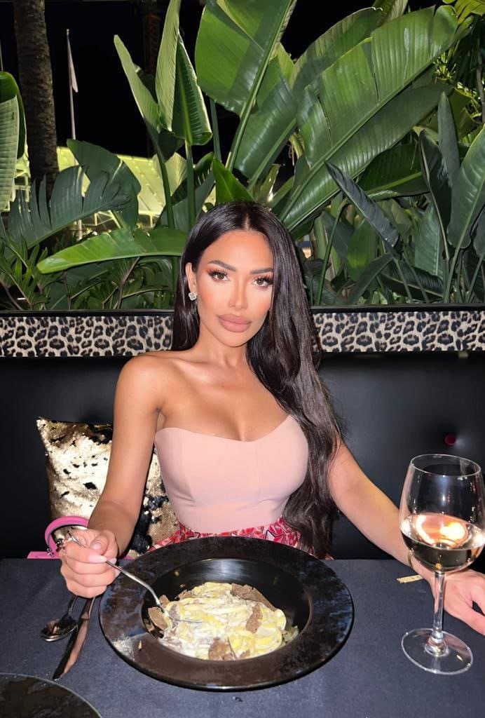 At a table with food, she wears a strapless pink top and patterned skirt.